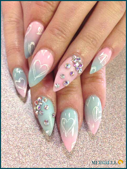 Diseño de uñas acrílicas ombre rosa y azul con corazones y detalles de joyas.