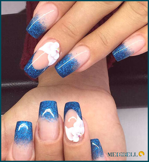 Diseño de uñas acrílicas ombre con purpurina azul con detalles florales.